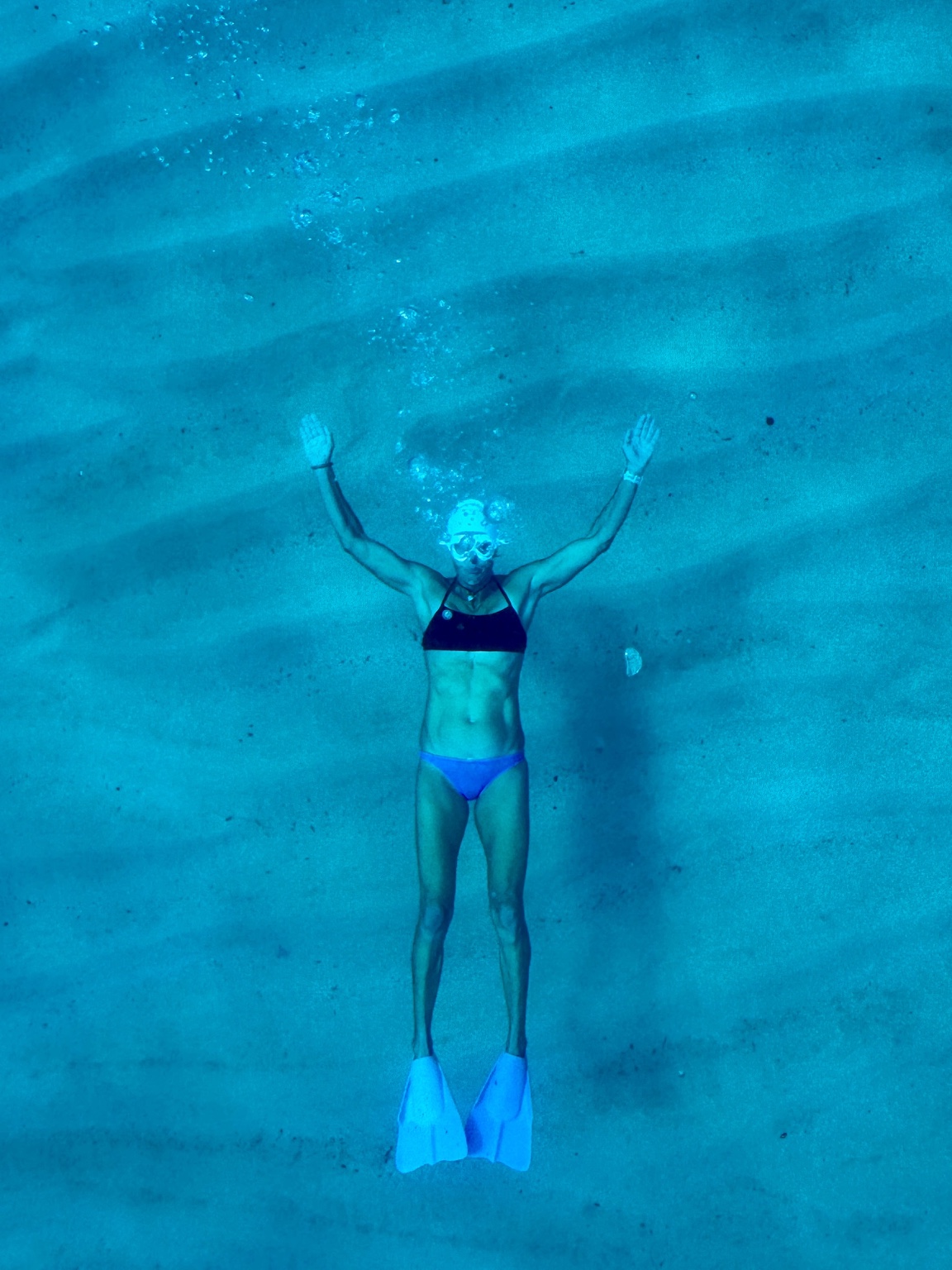 Heli underwater in a white swim cap and goggles, blowing bubbles